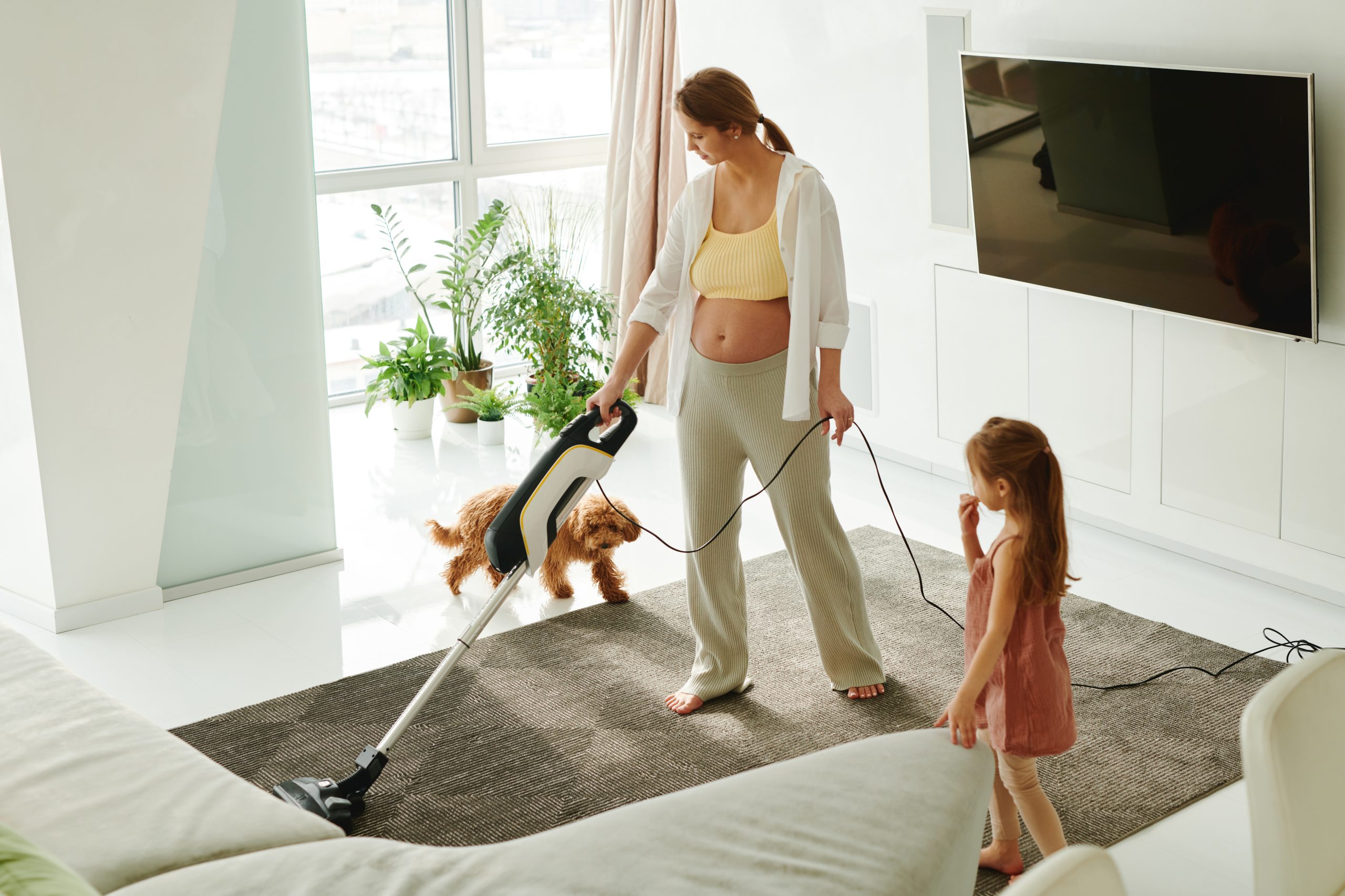 pregnant woman vacuuming with a child and dog.